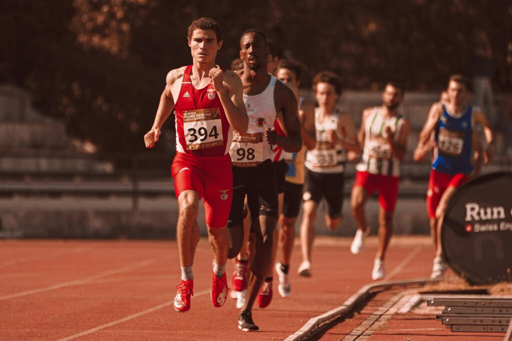 Group of athletes competing in a track and field race on an outdoor track under sunlight.