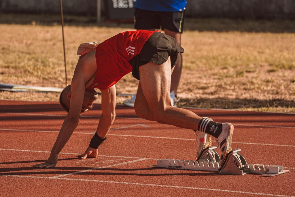 Athlete in red preparing to sprint on an outdoor track field. Focus on starting technique.