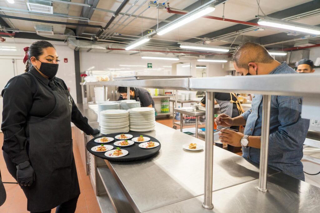 Chefs in a bustling kitchen preparing and plating dishes on a busy workbench.