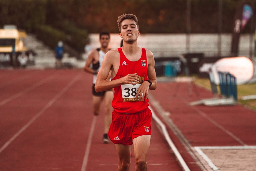 Exhausted male runner in red sports attire on track during daytime race, showcasing endurance and fitness.